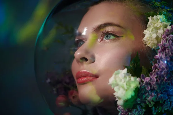 Air pollution, environmental disaster. Beautiful girl in a spacesuit filled with flowers looks up with hope on green background of outer space.