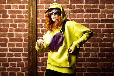 Sarı kapüşonlu modern hip-hop dansçısı kız çağdaş sokak dansı yapıyor. Tuğla duvar arkaplanı.