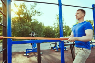 Açık spor salonunda çalışıyorum. Yakışıklı kaslı adam dışarıda spor salonunda elastik bantla güç egzersizleri yapıyor. Aktif sağlıklı yaşam tarzı. 