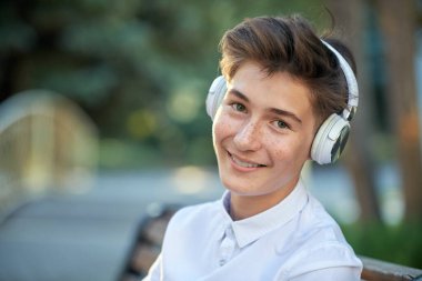 Mutlu insanlar konsepti. Bir yaz günü parkta oturan, kulaklıkla müzik dinleyen ve gülümseyen yakışıklı bir gencin portresi..