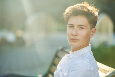 Güneşli bir yaz gününde parkta oturup kameraya bakan sakin ve ciddi bir gencin portresi. Modern nesil.