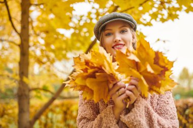 Mutlu sonbahar havası. Güz parkında elinde bir buket sarı akçaağaç yaprağıyla güzel genç bir kadın yürüyor.. 
