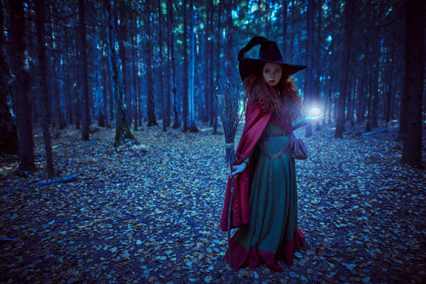 Fabulous young girl witch with magic ball and a broom in a deep forest. Fairy tales. Halloween.