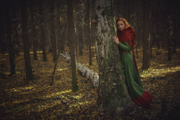 A beautiful red-haired girl of the Middle Ages walks through the forest. Celtic culture. Fantasy world.