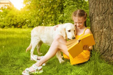 Neşeli şirin kız güneşli bir yaz parkında evcil köpeğine kitap okuyor. Parkta vakit geçirmek. Yaz tatili.