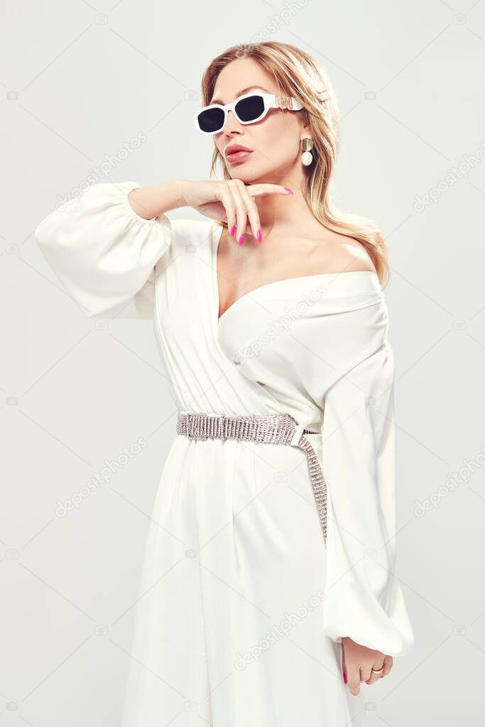 Beauty, fashion. Portrait of a stylish sexy middle aged woman in a white suit, precious jewelry and sunglasses on a white background.