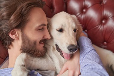 Evcil köpeği Golden Retriever ile evdeki kanepede yatan mutlu genç adam. Portreyi kapat.