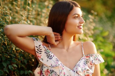 Romantik genç kadın parkta çiçekli bir elbiseyle poz veriyor ve gülümsüyor. Yaz modası ve güzellik. Açık hava portresini kapat.