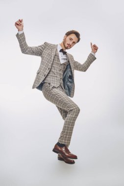 Klasik üç parçalı takım elbiseli yakışıklı bir gencin beyaz bir arkaplanda poz verirken tam boy portresi. Dans eden beyefendi. Erkek modası ve aksesuarları. 