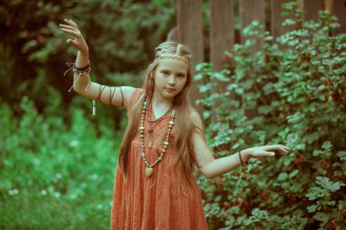 Hippi tarzı giyinmiş, yeşil çalıların arkasında poz veren şirin bir kızın portresi. Romantik hippi tarzı.