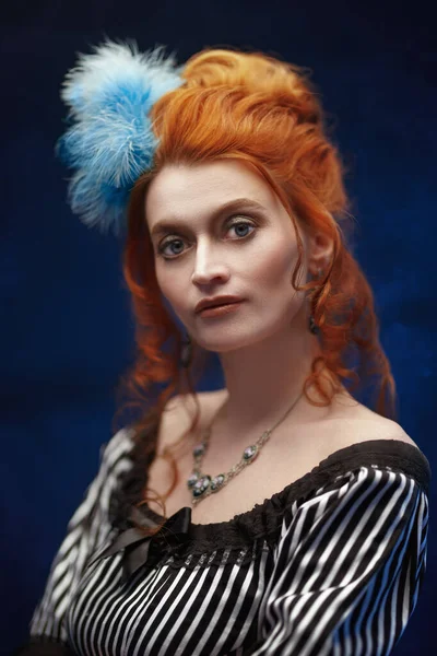 Portrait of a beautiful red-haired woman in a 19th century dress on a dark blue background. Fashion history, makeup and hairstyle.