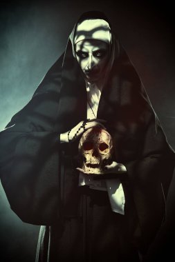 Cadılar Bayramı ve Korku. Elinde kafatası olan şeytani bir rahibe. Dumanlı arkaplan.