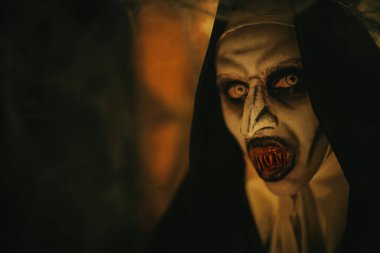 Turuncu ışıklı korkunç dişleri olan şeytani korkunç bir rahibenin yakın plan portresi. Cadılar Bayramı ve Dehşet.