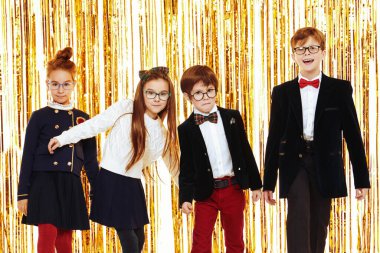 Zarif klasik okul üniformalı bir grup mutlu çocuk arka planda parlak altın folyo perdelerle poz veriyorlar. Çocuk partisi. Çocuk modası ve tatiller.