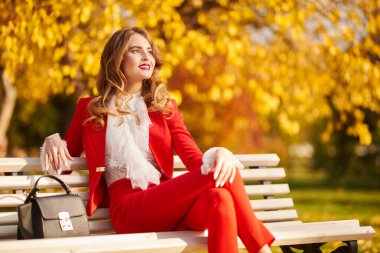 Güzel bir sonbahar parkındaki bankta dinlenen büyüleyici genç bir kadın. Güzellik, moda.