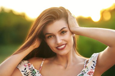 Açık havada gülümseyen genç bir kadının portresini çek ve parkta çiçekli bir elbiseyle gülümse. Yaz modası ve güzelliği.