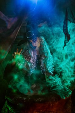 Korkunç yaşlı cadı, sihirli yeşil ışıkla çevrili kazanında iksir yapıyor. Cadılar Bayramı. Korkunç hikayeler..