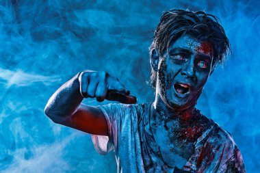 Cadılar Bayramı. Mavi ışıkta duman altında kalmış saldırgan, korkunç bir zombi gencin portresi. Korku filmi.