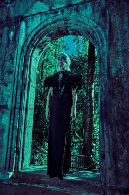 Uzun bir portre, zengin siyah elbiseli aristokrat bir dul kadın turkuaz ışıklandırmalı bir mezarlıkta üzgün duruyor. Kara Dul. Gizemciliğin atmosferi. Cadılar Bayramı.
