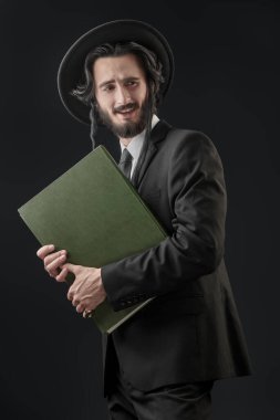 Happy Orthodox Jewish man holding talmud in his hands. Studio shot on a dark blue background.  clipart
