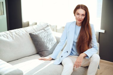 Çekici kızıl kız oturma odasındaki kanepede poz veriyor ve gülümsüyor. Mutlu insanlar ve yaşam tarzı konsepti. 