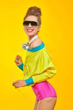 Renkli elbiseli duygusal güzel kız kulaklıkla poz veriyor. Parlak makyaj ve giysiler. Aktif yaşam tarzı, disko ve parti.