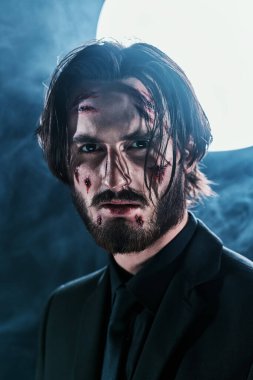 Yüzünde yaralar olan tehlikeli bir adamın yakın plan portresi dumanlı ayın arka planında..