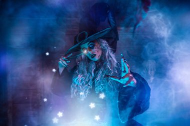 Korkunç yaşlı cadı sihirli mavi ışıkla çevrili sihirli bir değnekle kazanda iksir yapıyor. Cadılar Bayramı. Korkunç hikayeler..