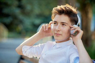Mutlu insanlar konsepti. Bir yaz günü parkta oturan, kulaklıkla müzik dinleyen ve gülümseyen yakışıklı bir gencin portresi..