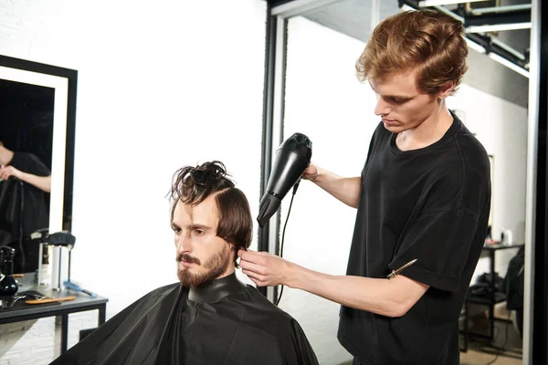 Master barber does the hairstyle and styling with dryer, dries hair to a handsome male client. Barbershop.