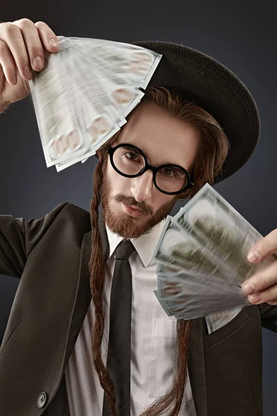 Portrait of a wealthy Jewish man with  a bundle of banknotes. Rich Jew concept. Studio shot on a dark blue background.
