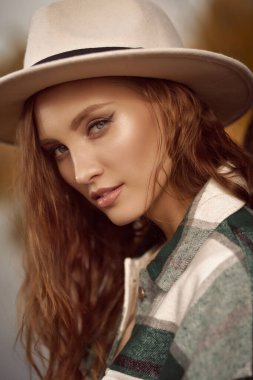 Sonbahar güzeli kadın. Sonbaharın arka planında keçeli şapka ve kareli fanila gömlekli güzel bir kızın portresi. Sonbahar renkleri.