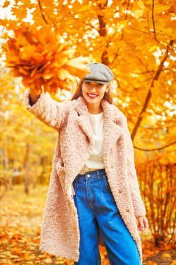 Güzel genç bir kadın elinde bir buket sarı akçaağaç yaprağıyla sonbahar parkında yürüyor. Mutlu sonbahar havası. 