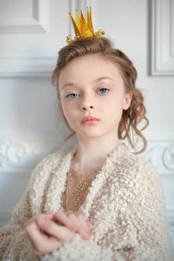 Beyaz klasik apartman dairesinde şenlik elbiseli ve taç giyen güzel küçük kız prenses duruyor. Çocukluk hayalleri. Peri masalları.