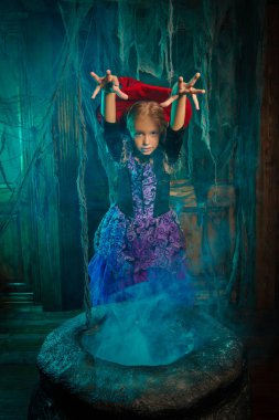 Eski evdeki yanan kazanda bir cadının kostümünü giyen sevimli küçük bir kız. Cadılar Bayramı.