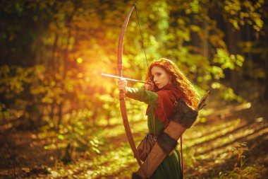 Orta Çağ 'dan güzel kızıl saçlı okçu kız sonbahar ormanında duruyor ve bir yay fırlatıyor. Kelt kültürü. Hayal dünyası..