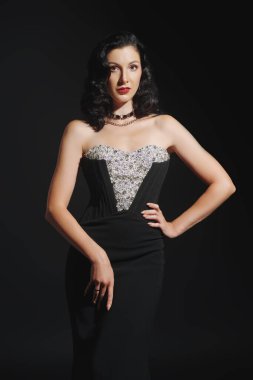 Zarif bir gece elbisesi ve siyah bir arka planda mücevherleri olan güzel bir esmer kadının portresi. 30 'lar-40' lar tarzında akşam modası. Stüdyo çekimi.  