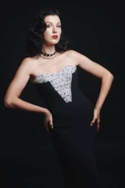 Zarif gece elbisesi ve siyah arka planda mücevherleri olan çekici esmer kadın. Makyaj ve saç stili 30 'lardan 40' lara kadar. Moda stüdyosu çekimi.  