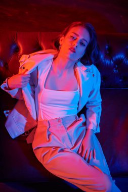 Çekici esmer bir kadının portresi. Kırmızı ışıklı, karanlık bir odada, kanepede oturuyor. Büyüleyici yaşam tarzı, lüks.. 