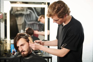 Berber dükkanında müşteriye hizmet eden bir kuaför. Yakışıklı esmer adam kuaförde kuaförü ziyaret ediyor..