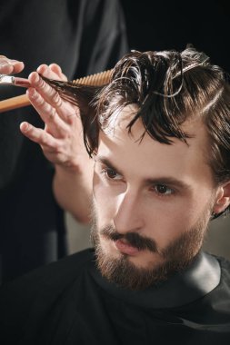 Bir berber dükkanında saçını kestiren yakışıklı bir esmerin yakın plan portresi. Erkek güzelliği ve tarzı. 