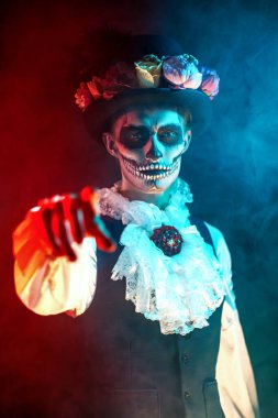 Ölü Karnaval Günü. Kameraya bakan, geleneksel Meksika kostümlü, şeker kafalı yakışıklı bir adam. Esrarengiz sis ve kırmızı ışıkla siyah arkaplan. Cadılar Bayramı.