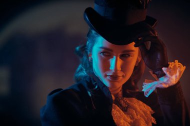 19. yüzyıldan kalma takım elbiseli zarif bir bayan karışık renkli ışıkta koyu bir arka plana karşı. Tarihsel saç stili ve makyaj.