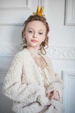 Beyaz klasik apartman dairesinde kafasına taç takmış, altından bir elbise ve ceket giymiş güzel küçük bir prensesin stüdyo portresi. Çocuk modası.. 