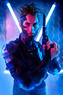 Neon ışıklı arka planda siber punk savaşçı portresi. Cesur bir siber punk koruyucu üniforma giymiş silahlı ve tetikte bekliyor. Oyun, sanal gerçeklik.