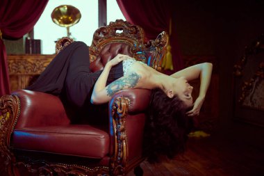 1930-1940 'ların klasik tarzı. Zarif bir akşamda çarpıcı esmer kadın kırmızı bir koltukta sırtı ağrırken poz veriyor. Kaliteli bir odanın içinde stüdyo portresi..   