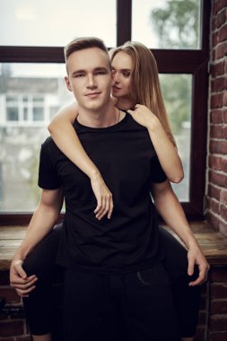 Mutlu genç aşıklar pencerede poz verip evde vakit geçiriyorlar. Çatı katı tarzı bir daire. Aşk ve ilişki. 