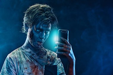 Cadılar Bayramı. Korkunç zombi çocuk akıllı telefonuyla selfie çekiyor. Boşluğu kopyala. 
