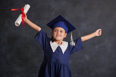 Okul ve Eğitim. Okul üniformalı ve akademik şapkalı mutlu küçük kız kara kara tahtaya karşı duruyor ve elinde diplomayla gülümsüyor. Metin için yer.