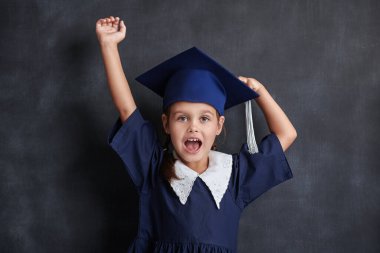 Okul üniformalı, akademik şapkalı, siyah bir tahtanın arkasında duran ve neşeyle bağıran küçük tatlı bir kız çocuğunun portresi. Eğitim.